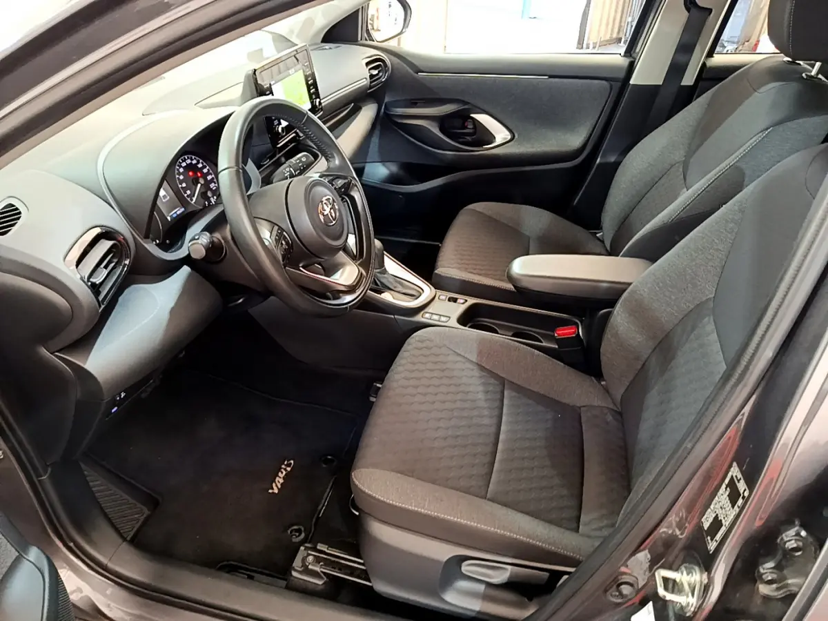 Intérieur avant droit d'une Toyota Yaris hybride gris clair, volant cuir, sièges tissu gris et écran tactile central.