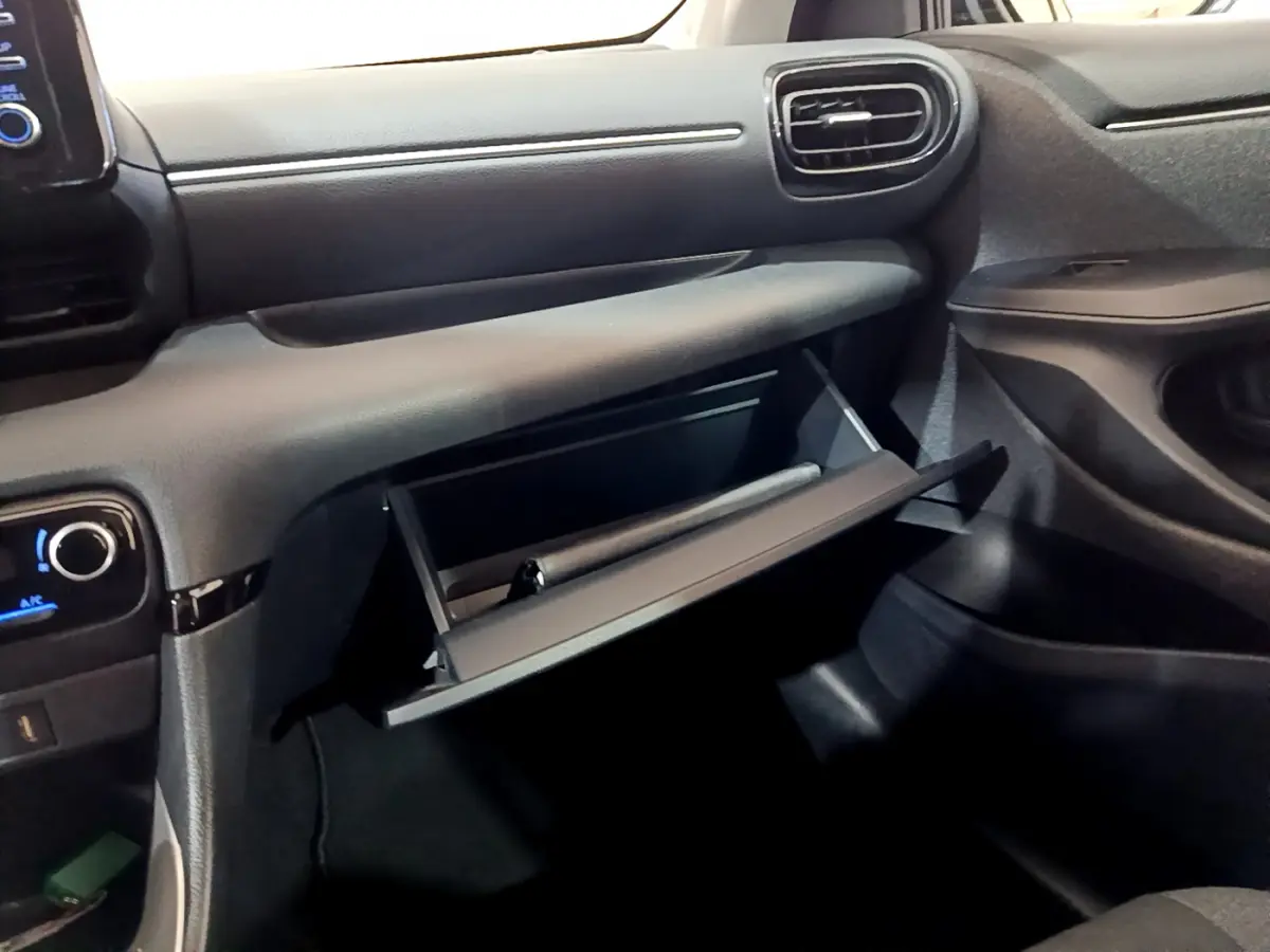 Intérieur de la Toyota Yaris hybride 2021, vue côté passager sur la boîte à gants ouverte et tableau de bord gris foncé.