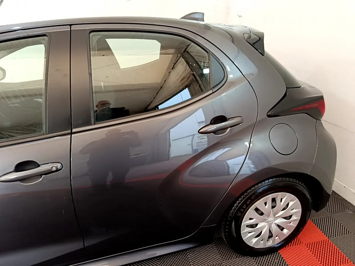 Vue côté droit arrière d'une Toyota Yaris hybride gris clair, mettant en valeur la porte arrière et la roue avec enjoliveur.