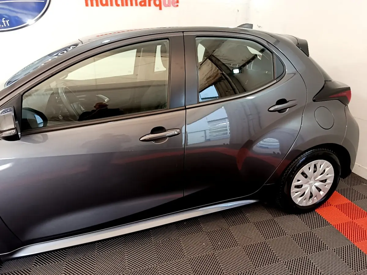 Profil côté gauche de la Toyota Yaris hybride gris clair 2021, avec jantes acier et poignées de porte assorties.