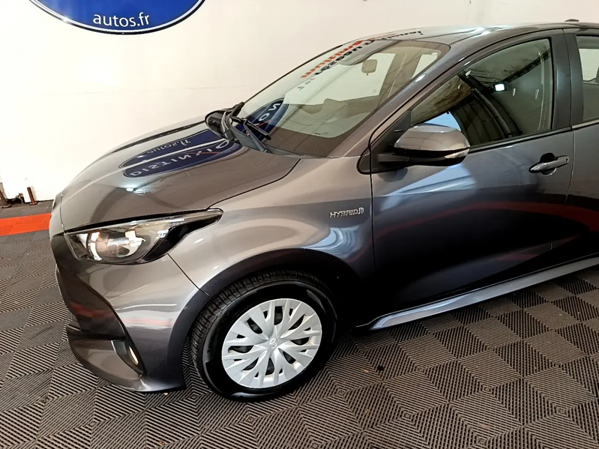 Vue 3/4 avant gauche d'une Toyota Yaris hybride gris clair avec jante acier et logo Hybrid sur l'aile avant.