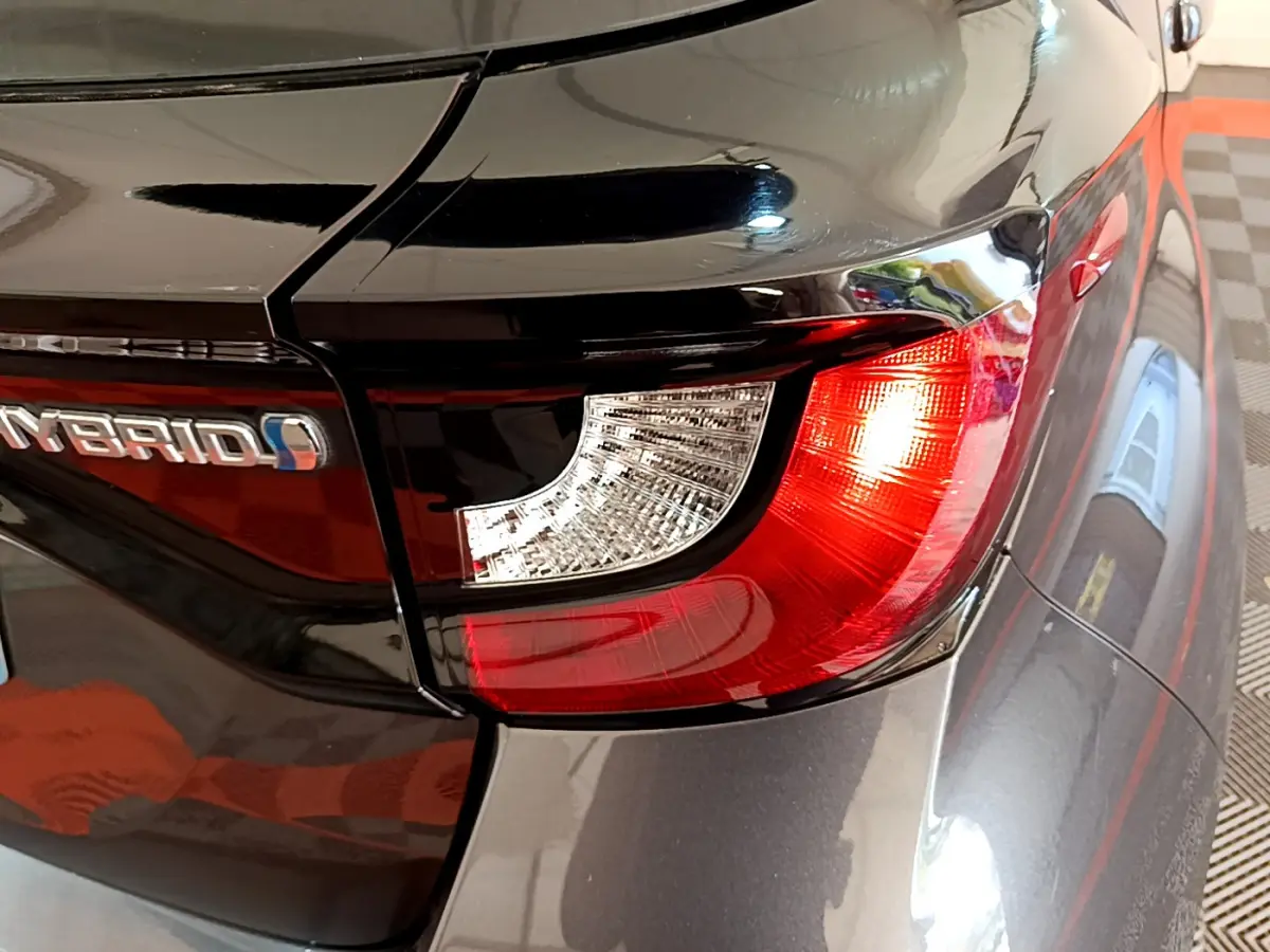 Gros plan sur le feu arrière droit rouge et blanc d'une Toyota Yaris hybride gris clair avec logo Hybrid visible.