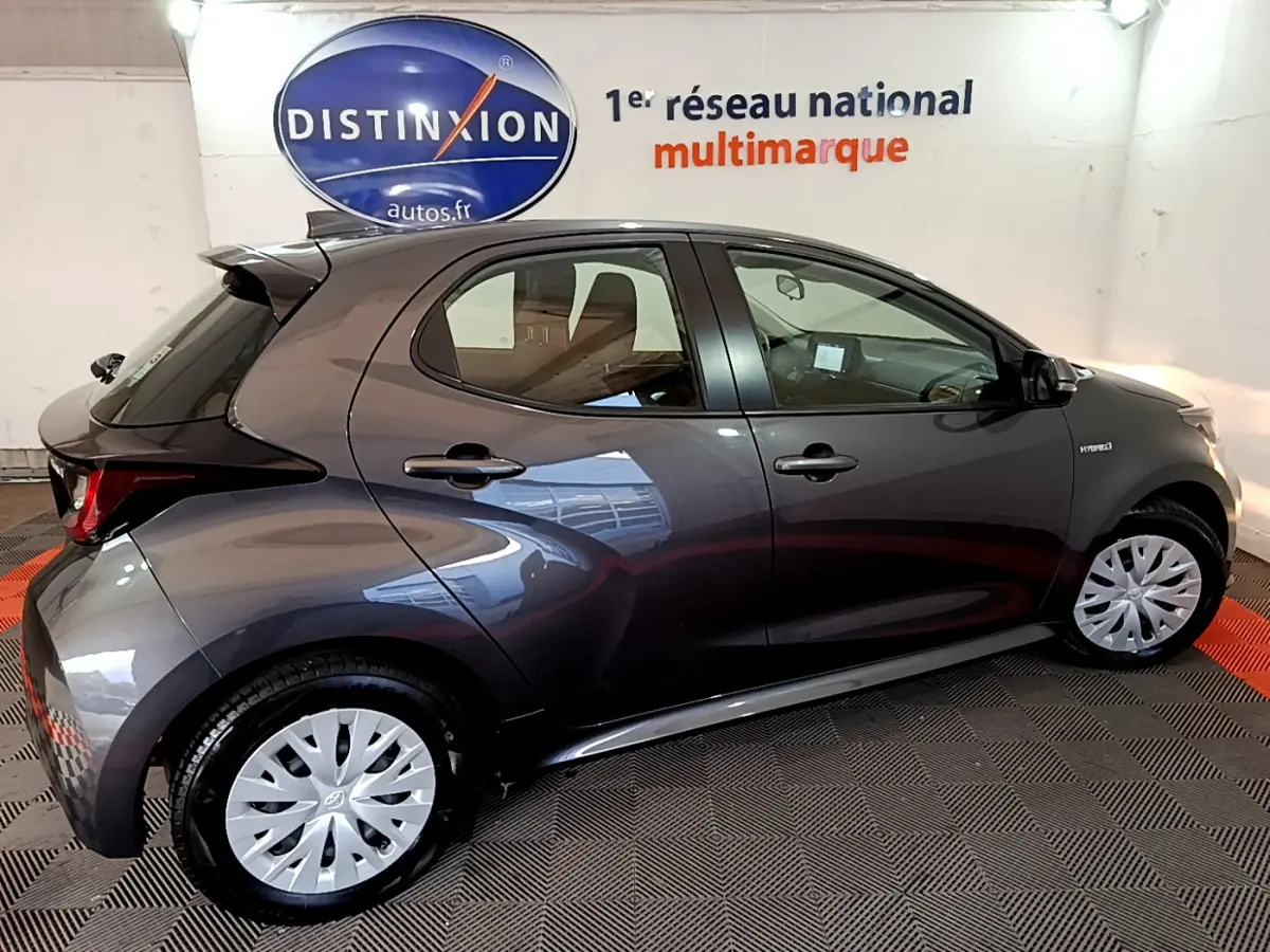 Profil côté gauche d'une Toyota Yaris hybride gris clair 2021 avec jantes et logo hybride visible sur l'aile avant.