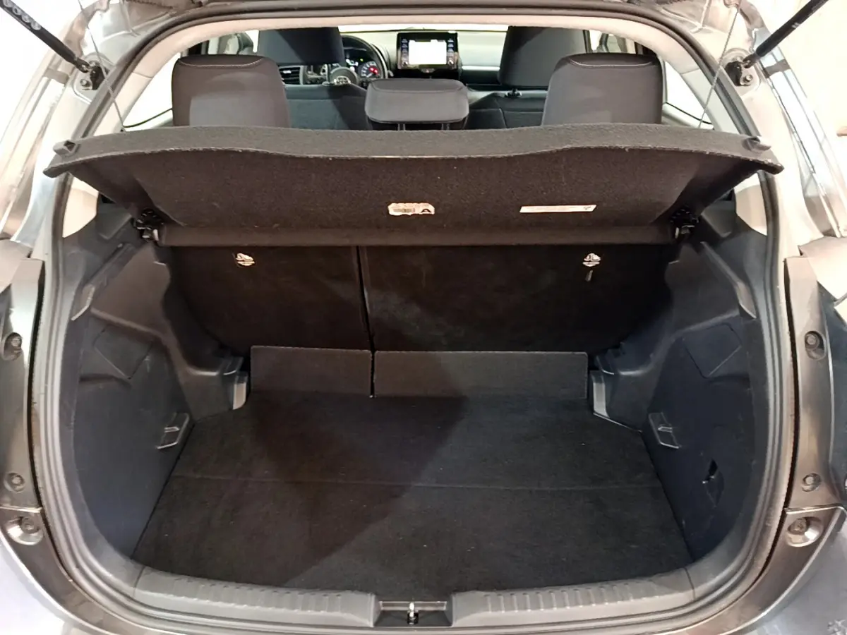 Coffre ouvert vu de l'arrière d'une Toyota Yaris hybride gris clair, banquette arrière et tableau de bord visibles.