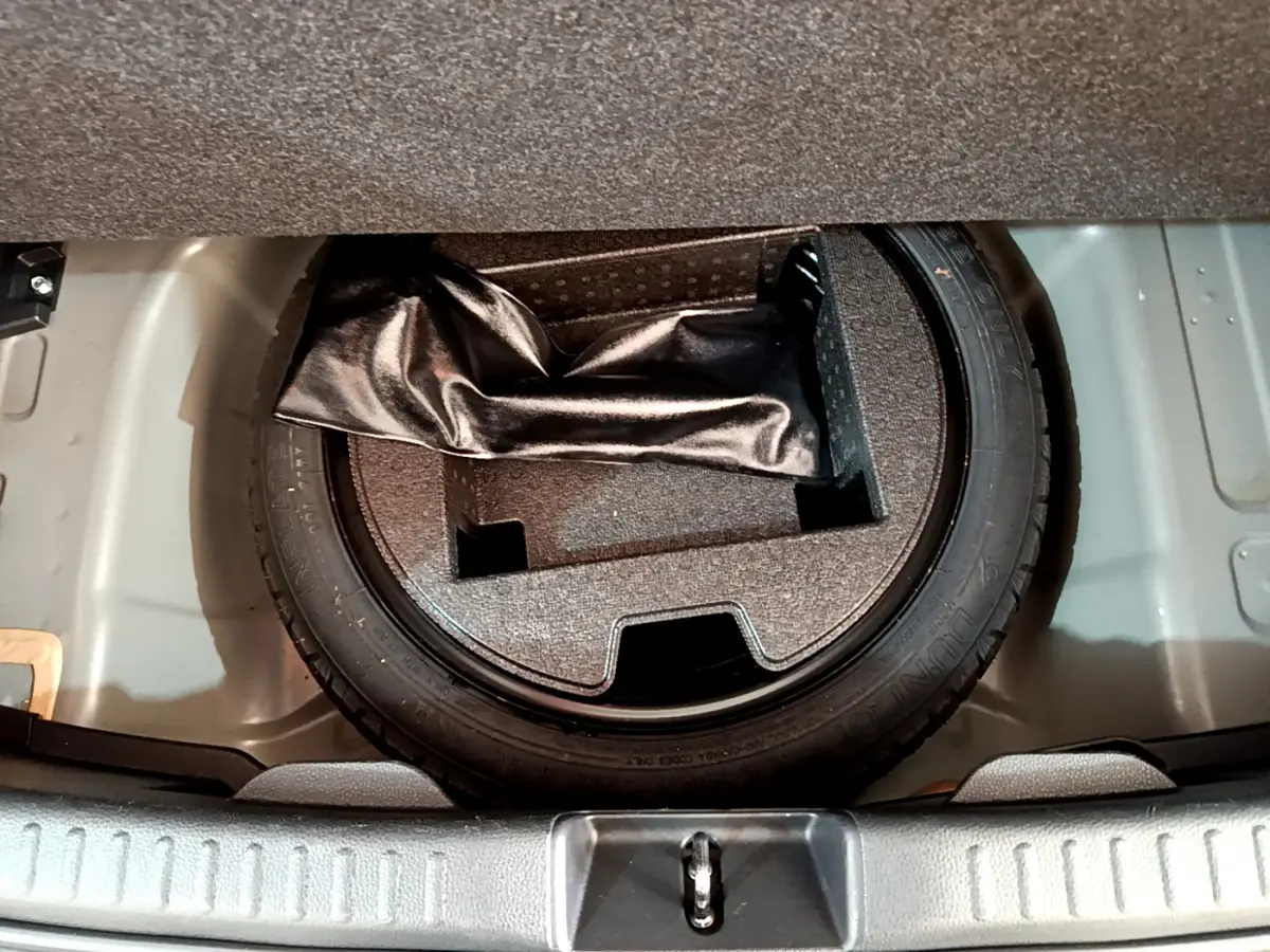 Vue plongeante sur la roue de secours et le rangement sous le plancher du coffre d'une Toyota Yaris gris clair hybride.
