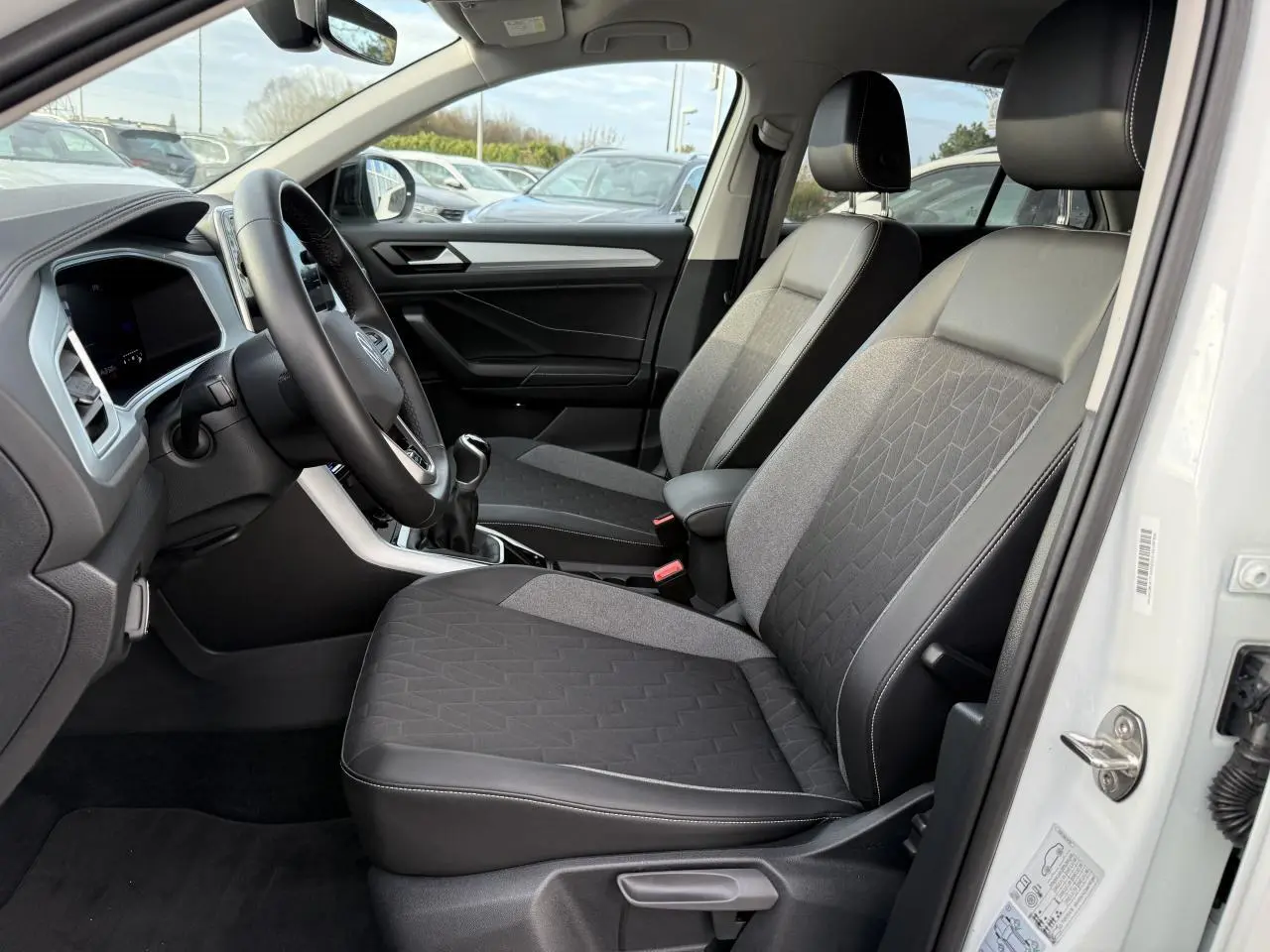 Intérieur côté conducteur du Volkswagen T-Roc blanc 2025, sièges tissu et cuir, volant multifonction et boîte manuelle visible.