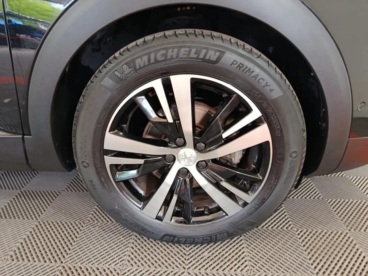 Gros plan sur la roue avant gauche noire du Peugeot 3008 PureTech 130 GT avec jante alliage bicolore et pneu Michelin.
