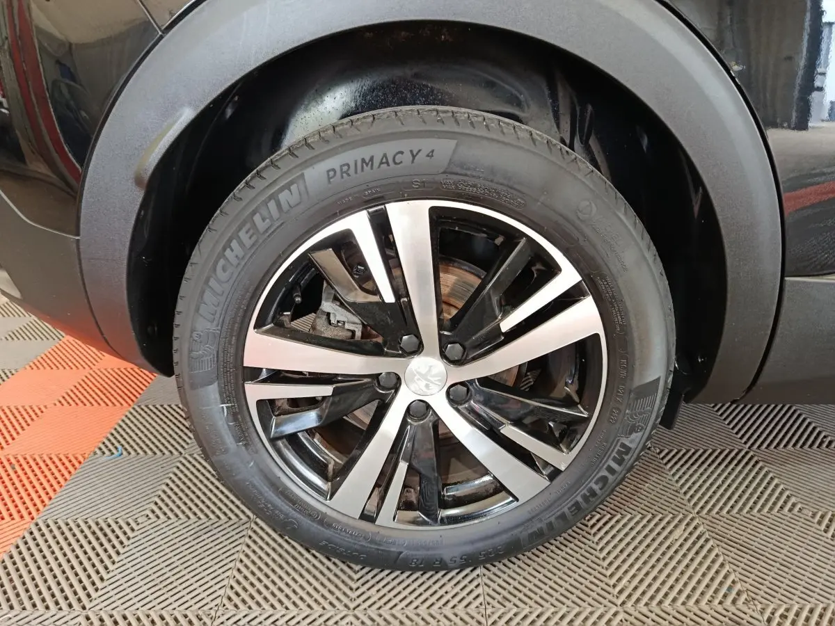 Gros plan sur la roue avant gauche noire du Peugeot 3008 PureTech 130 GT avec jante alliage bicolore.