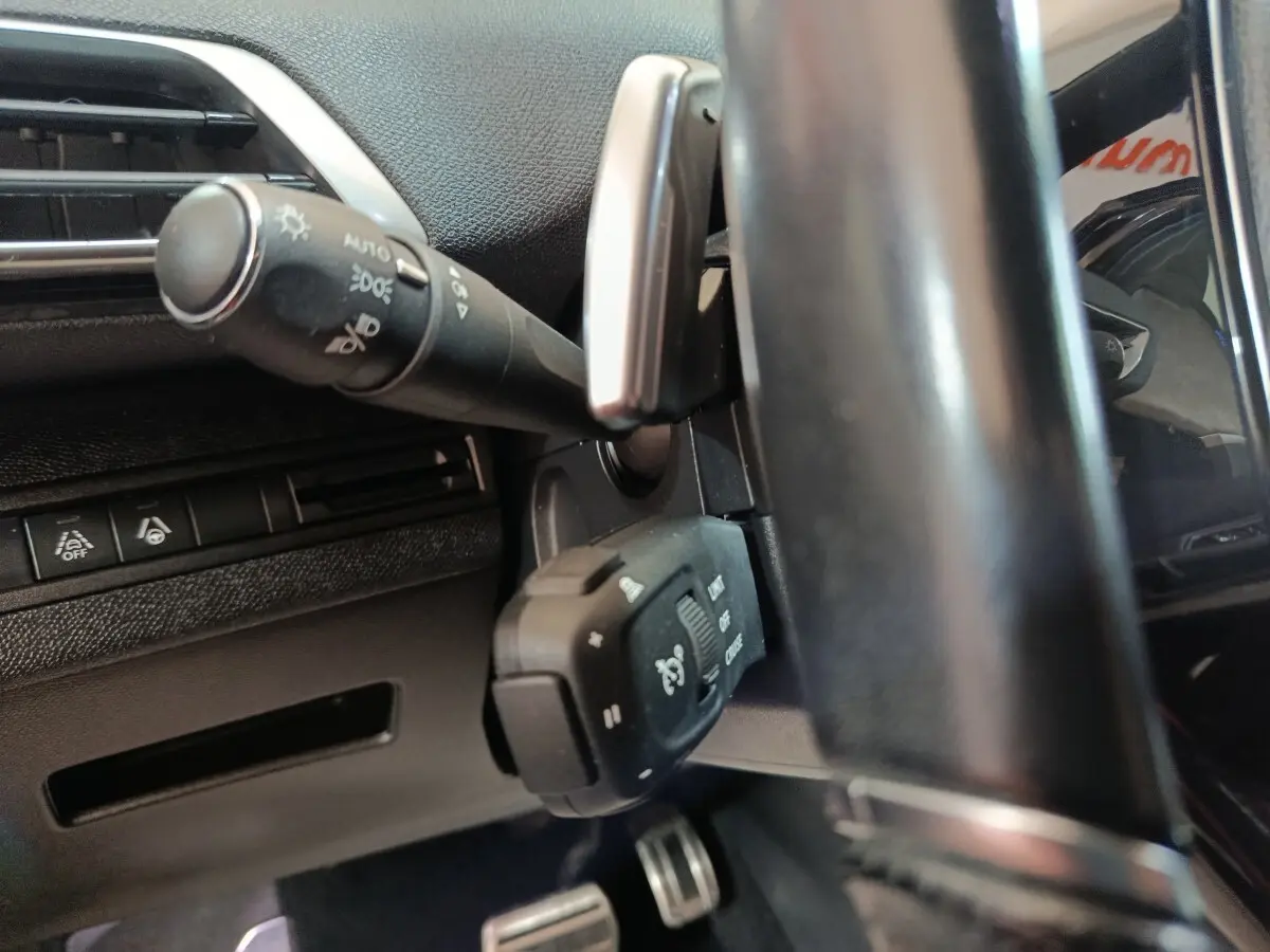Gros plan sur la colonne de direction et commandes au volant du Peugeot 3008 noir, intérieur avec volant cuir.