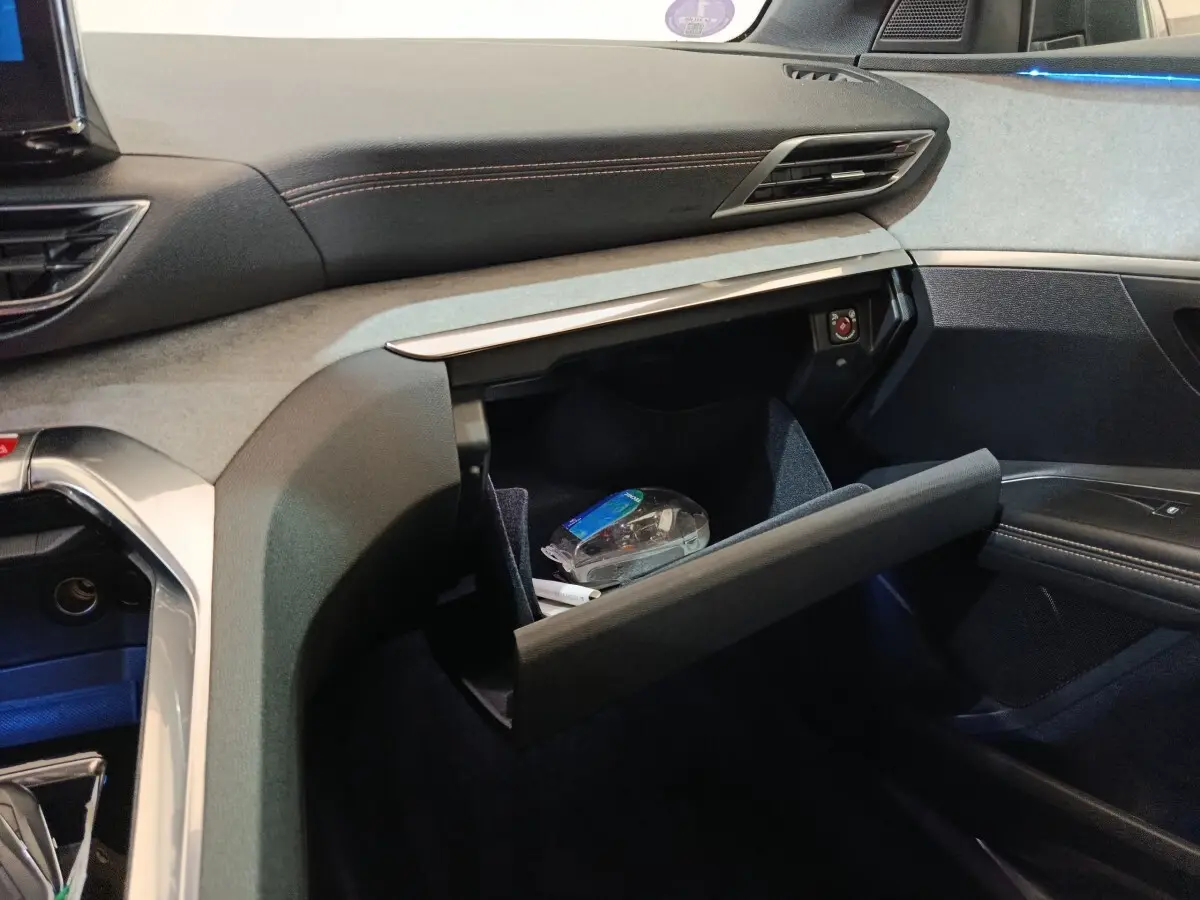 Intérieur côté passager du Peugeot 3008 GT 2022 noir, boîte à gants ouverte avec objets visibles et éclairage d'ambiance bleu.