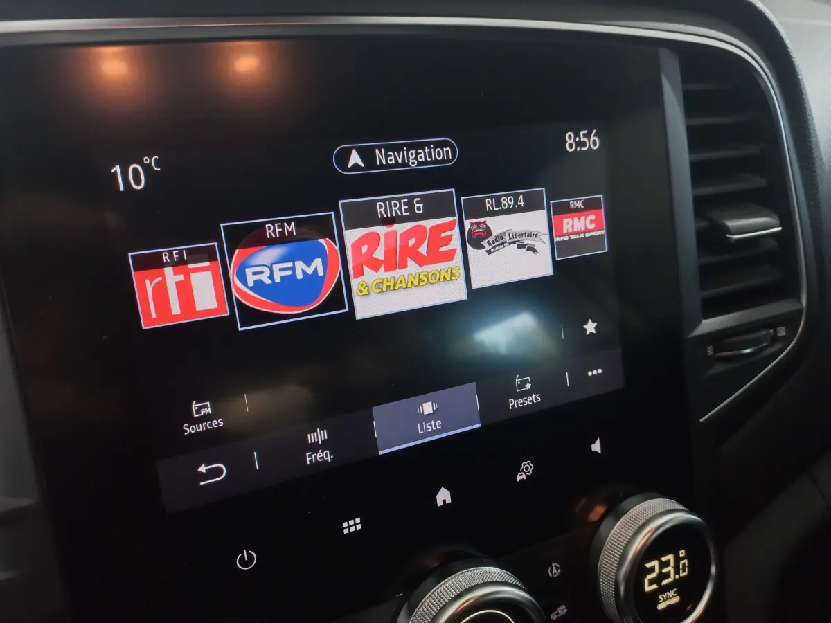 Écran tactile central de la Renault Mégane Business blanc, affichant les stations radio avec commandes climatisation en dessous.