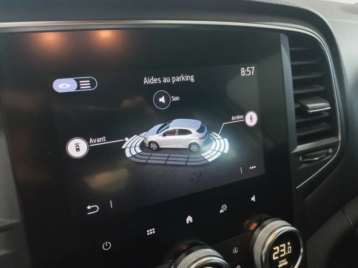 Écran tactile intérieur affichant l'aide au parking d'une Renault Mégane Business blanche, avec commandes climatisation visibles.