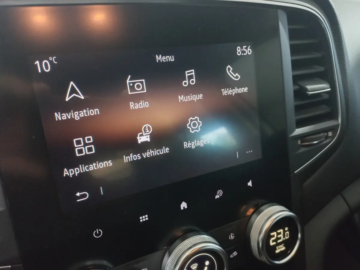 Écran tactile central affichant menu multimédia et climatisation digitale dans Renault Mégane Business blanc, vue de face rapprochée.