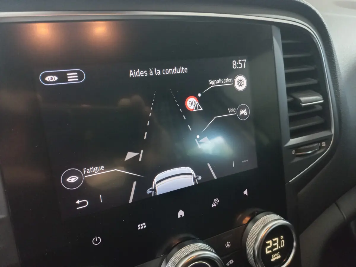 Écran tactile central de la Renault Mégane Business blanc, affichant les aides à la conduite et la climatisation à 23°C.