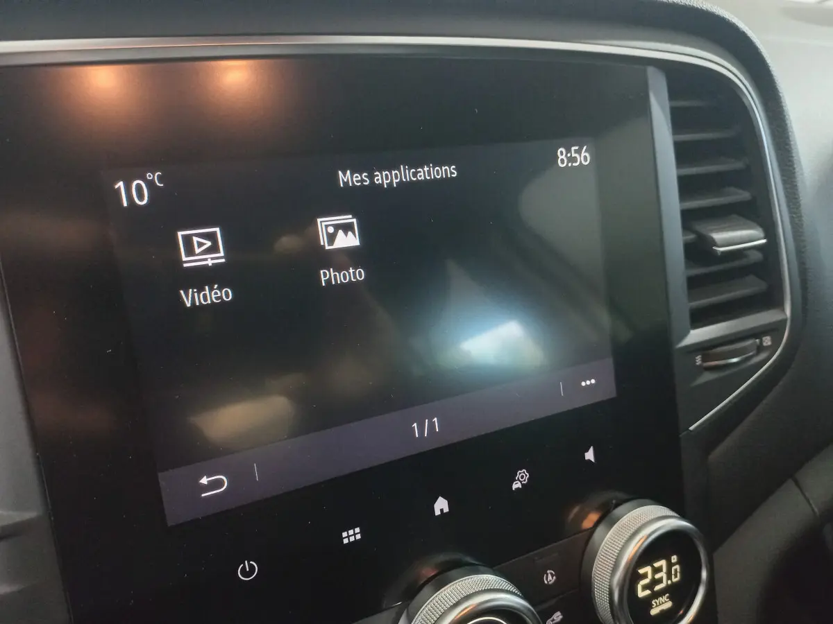 Écran tactile central affichant les applications vidéo et photo, avec commandes de climatisation digitale sur Renault Mégane blanche.