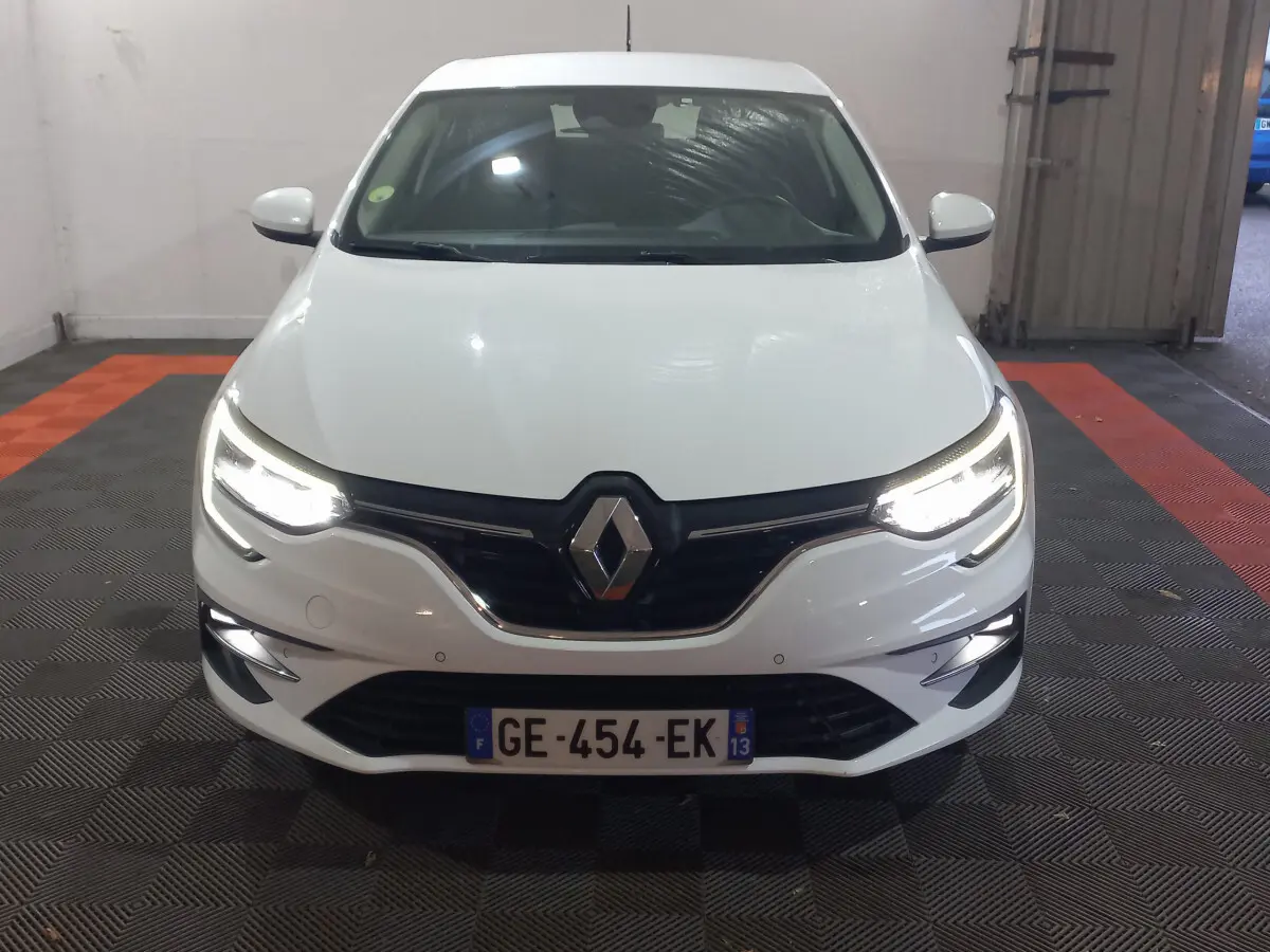 Vue frontale d'une Renault Mégane blanche 2022 avec phares LED allumés dans un garage.