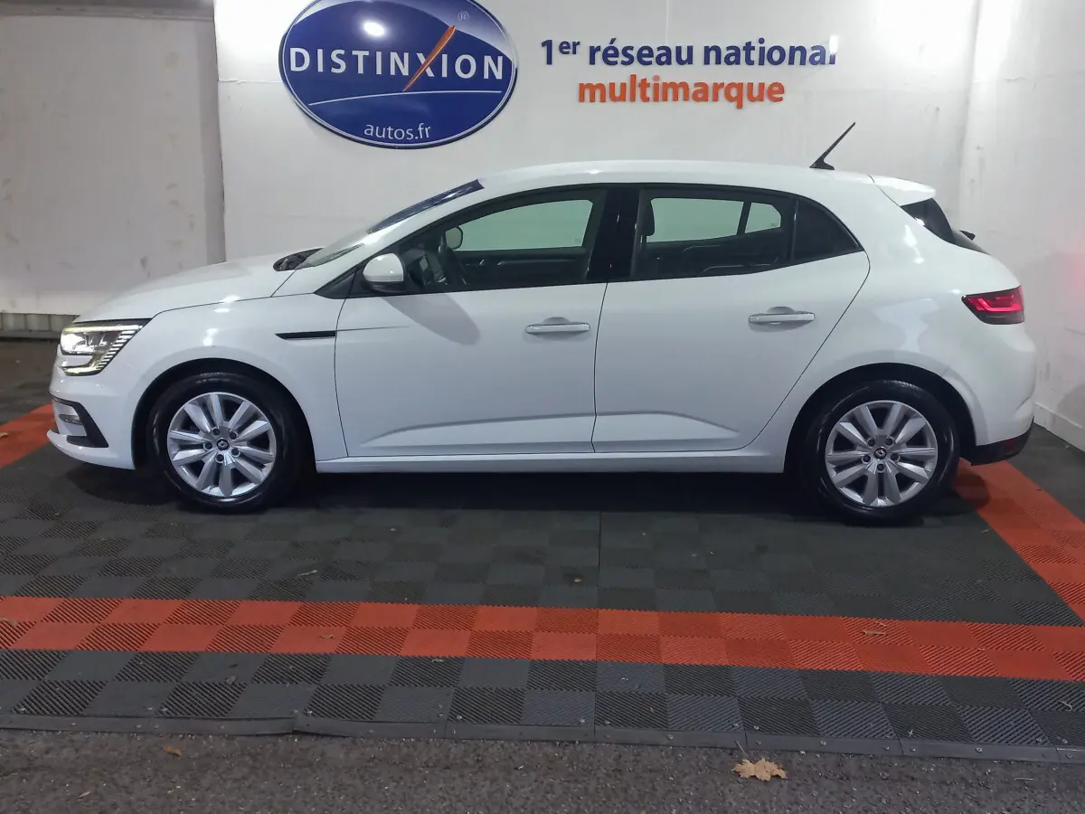 Profil côté gauche d'une Renault Mégane Business Blue dCi 115 EDC blanche, avec feux arrière allumés en intérieur showroom.