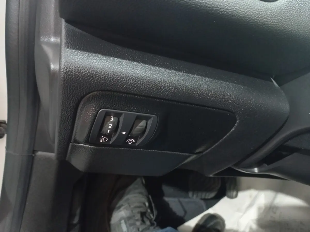Gros plan sur les commandes de réglage des phares et du tableau de bord dans une Renault Mégane Business blanche, côté conducteur.