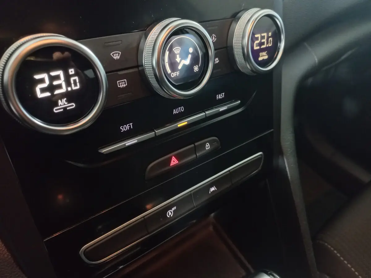 Gros plan sur la console centrale noire de la Renault Mégane Business, affichant la climatisation à 23°C et commandes tactiles.