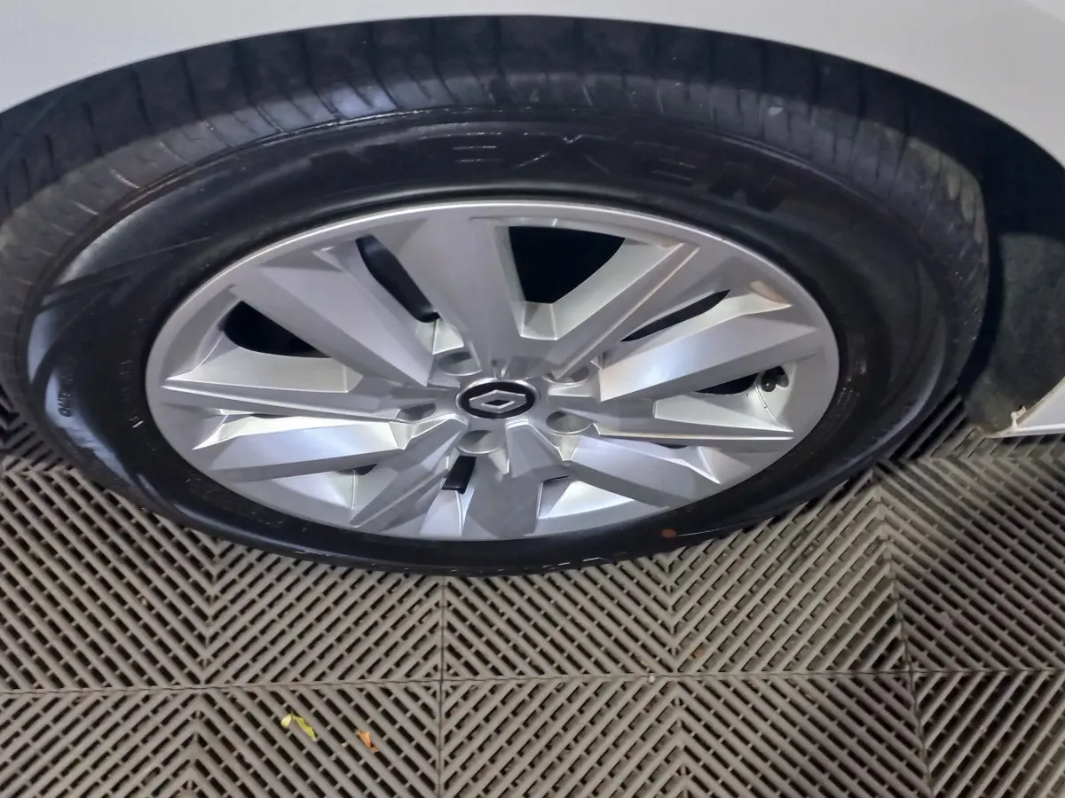 Gros plan sur la roue avant droite d'une Renault Megane blanche avec jante alu au design moderne.