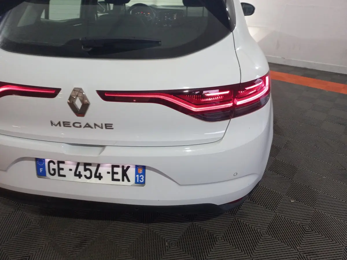Vue arrière d'une Renault Mégane blanche avec feux LED allumés et plaque d'immatriculation française visible