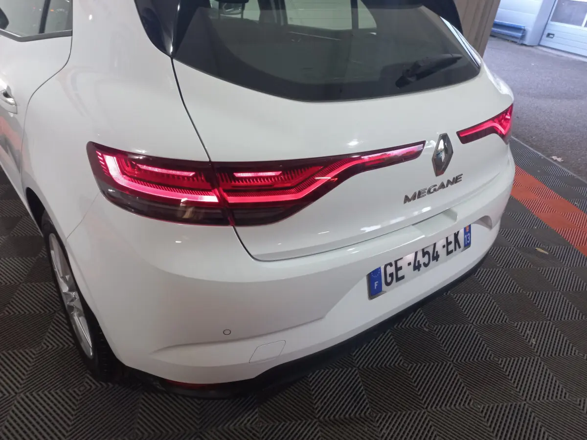 Vue 3/4 arrière droite d'une Renault Mégane blanche 2022 avec feux arrière LED allumés et plaque française visible