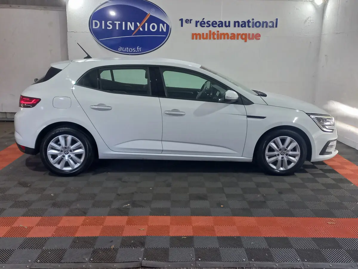 Profil droit d'une Renault Mégane Business Blue dCi 115 EDC blanche, stationnée en intérieur sur sol damier noir et orange.