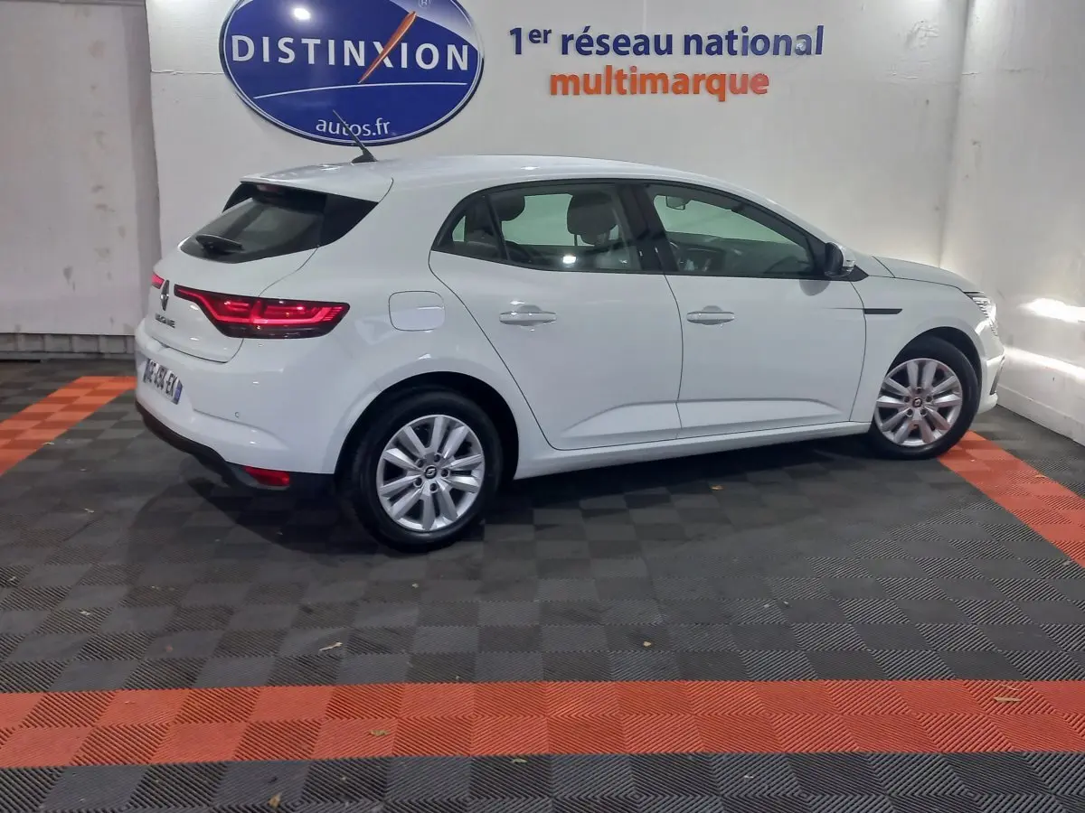 Vue latérale droite d'une Renault Mégane Business Blue dCi 115 blanche, avec feux arrière LED allumés, en intérieur showroom.