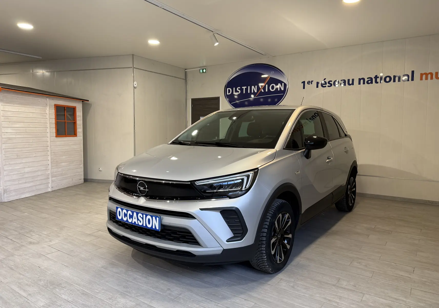 Vue 3/4 avant d’un Opel Crossland gris 2023 en showroom, avec calandre noire et jantes alliage noires.