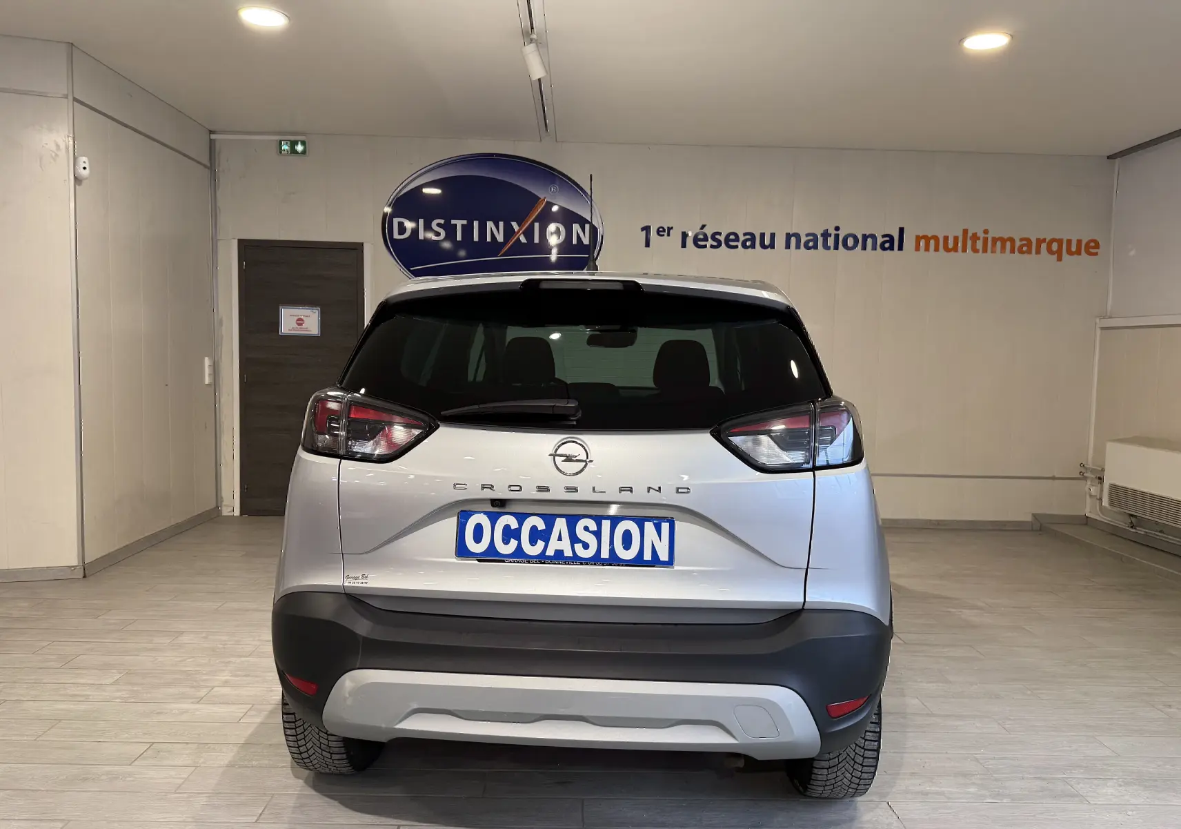 Vue arrière d'un Opel Crossland gris 2023 avec plaque "OCCASION" dans un showroom lumineux.