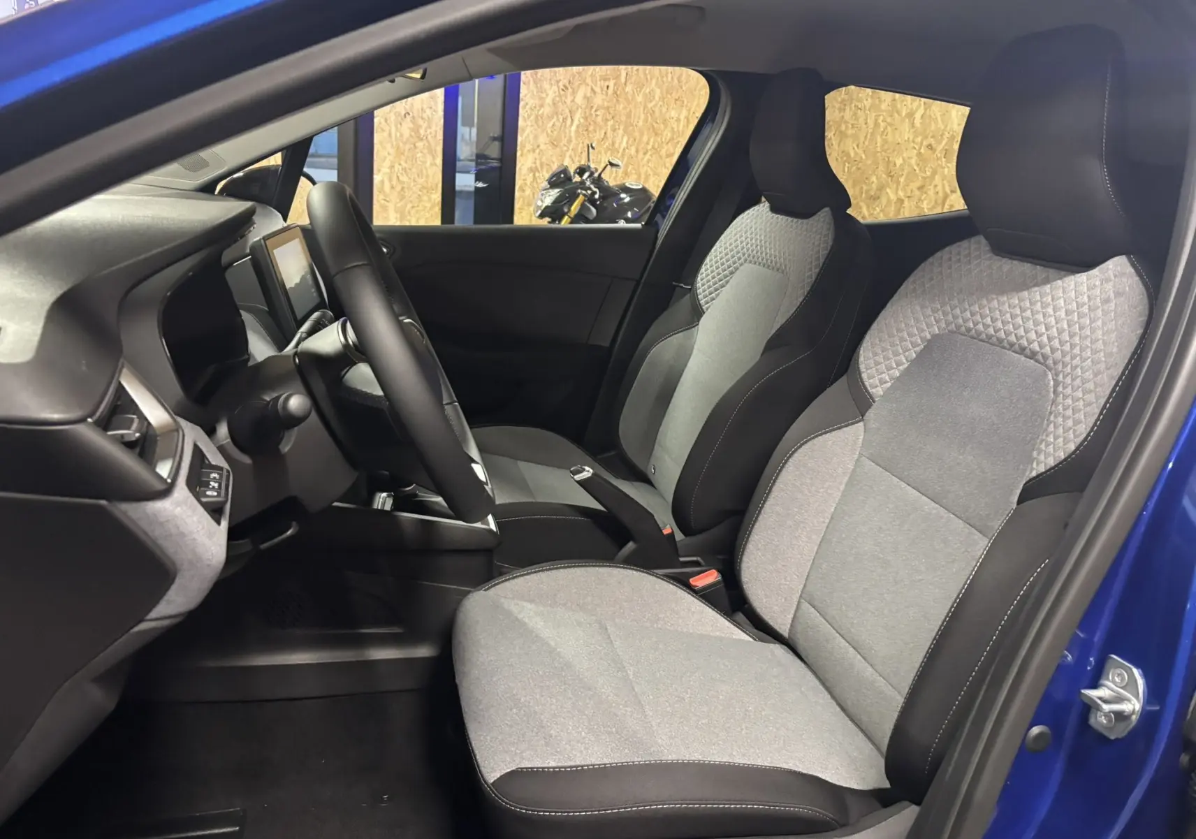 Vue intérieure côté gauche de la Renault Clio bleu iron 2024, mettant en valeur les sièges tissu gris clair et noir.