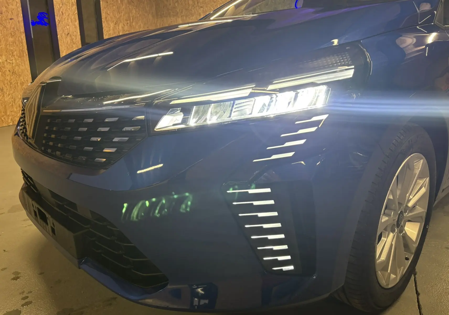 Vue 3/4 avant droit d'une Renault Clio 2024 bleu Iron avec phares LED allumés et calandre moderne.