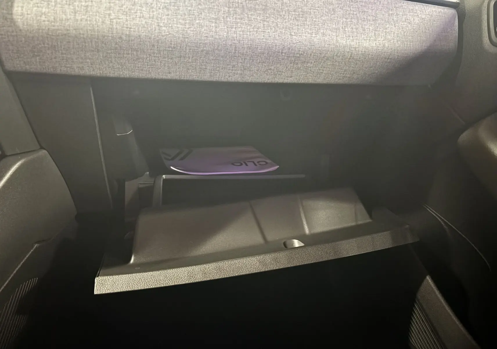 Gros plan sur la boîte à gants ouverte du Renault Clio 2024, intérieur gris et manuel visible à l'intérieur.