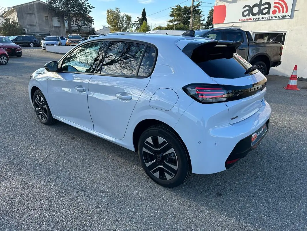 Peugeot 208 Hybrid blanc vue 3/4 arrière droit, jantes alliage noires, feux arrière LED et antenne requin visible.