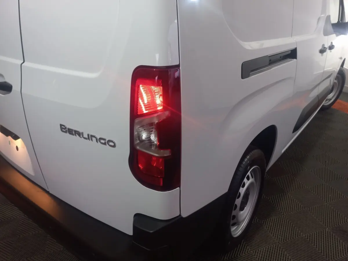 Vue arrière 3/4 droit d’un Citroën Berlingo blanc avec feu arrière allumé et logo Berlingo visible.