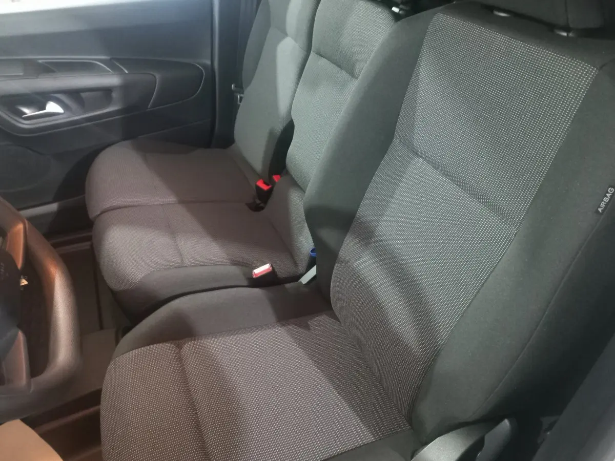 Vue intérieure côté conducteur du Citroën Berlingo XL 2025, sièges tissu gris foncé avec ceinture rouge visible.