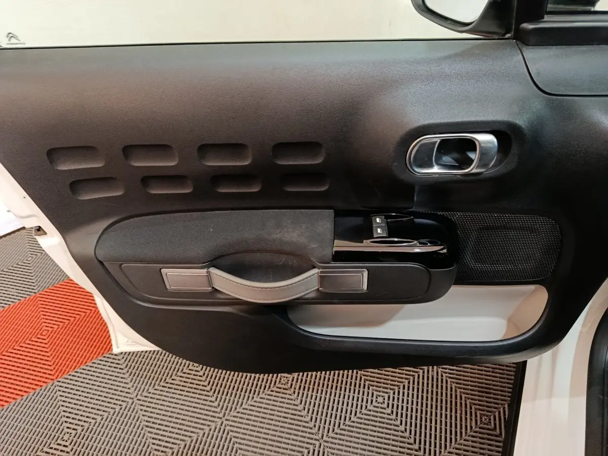 Vue rapprochée de la porte avant gauche blanche d'une Citroën C3 2021 avec poignée noire et commandes de vitres.