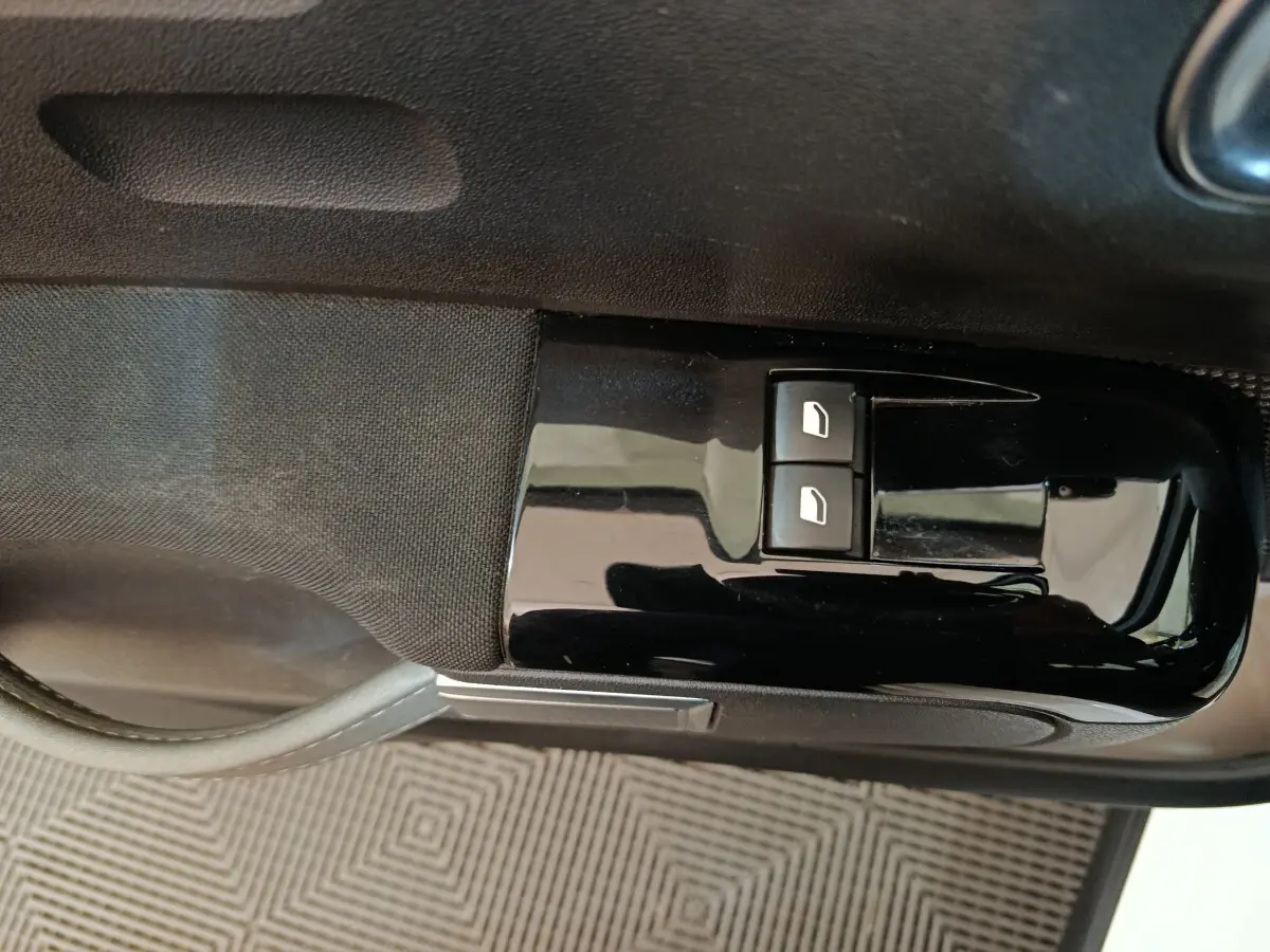 Gros plan sur les commandes de lève-vitres avant gauche en plastique noir brillant dans une Citroën C3 blanche de 2021.