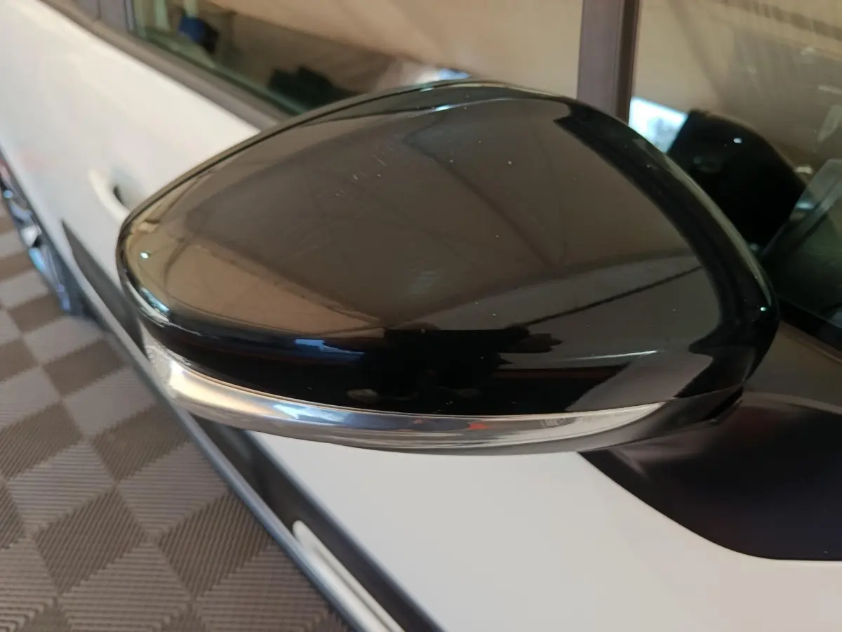 Gros plan sur le rétroviseur noir côté gauche d'une Citroën C3 blanche vue de profil, avec clignotant intégré.