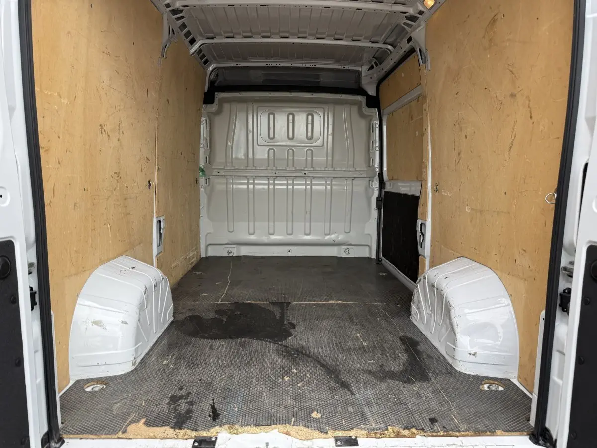 Vue intérieure arrière du fourgon blanc Peugeot Boxer 2.2 140 CH avec parois en bois et sol noir usé.