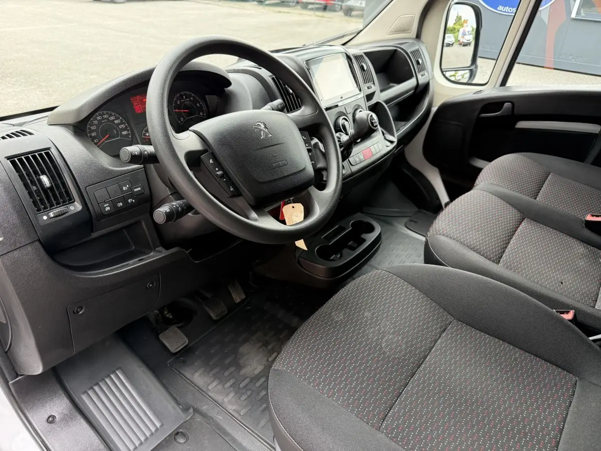 Vue intérieure côté conducteur du Peugeot Boxer Fourgon 2023, volant multifonctions et sièges tissu gris à motifs rouges.