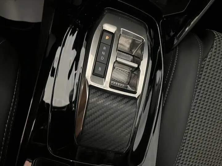 Gros plan sur la console centrale de la Peugeot e-208 GT 2022 avec levier de vitesses automatique et finition carbone.