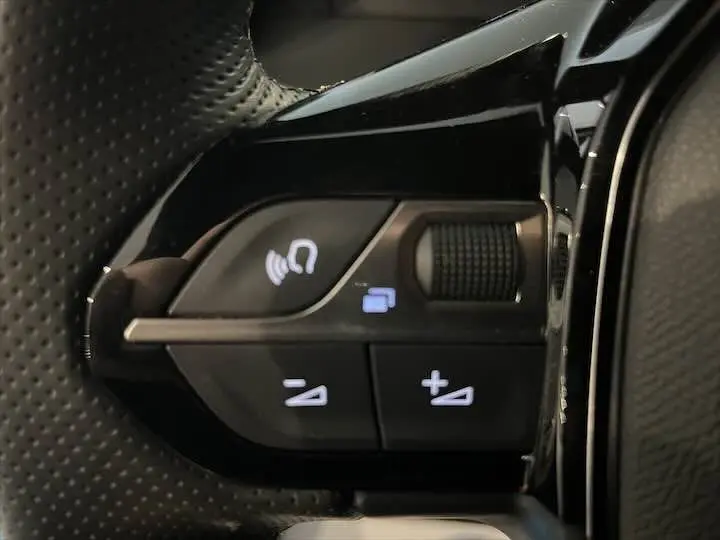 Gros plan sur les commandes de volume et téléphone au volant cuir perforé de la Peugeot 208 électrique gris Artense.