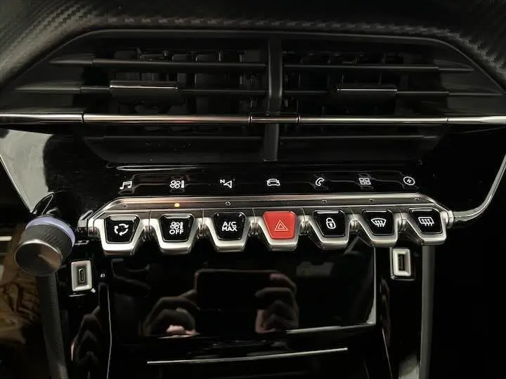 Vue rapprochée de la console centrale noire brillante de la Peugeot e-208 GT avec boutons de commande et aérateurs.