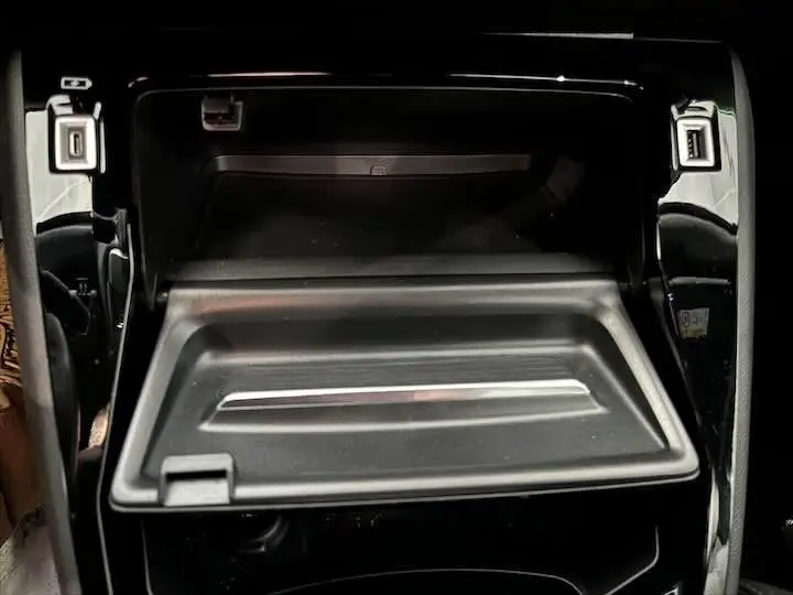 Gros plan sur la boîte à gants ouverte de la Peugeot 208 E-208 GT 2022 avec finition noire brillante.