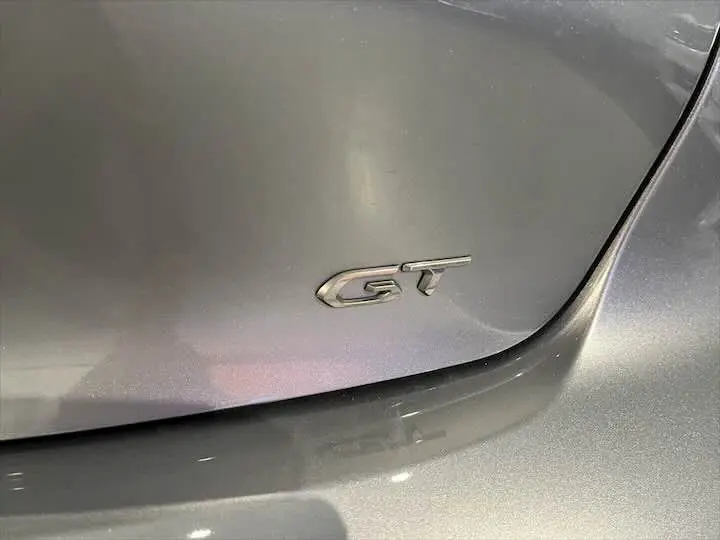 Gros plan sur l'emblème GT argenté sur la carrosserie gris artense d'une Peugeot 208 électrique.