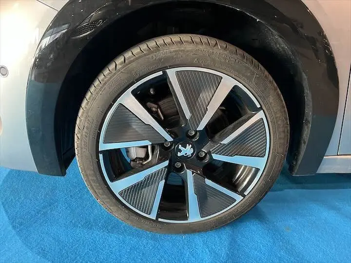 Gros plan sur la roue avant droite d'une Peugeot 208 électrique gris Artense, mettant en valeur la jante moderne bicolore.