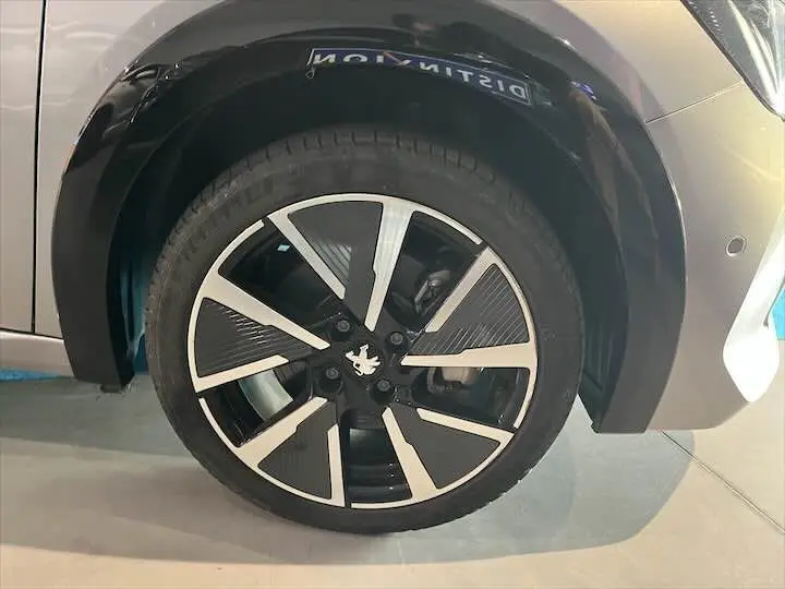 Gros plan sur la roue avant droite d'une Peugeot 208 E-208 GT gris Artense avec jante noire et argentée au design moderne.