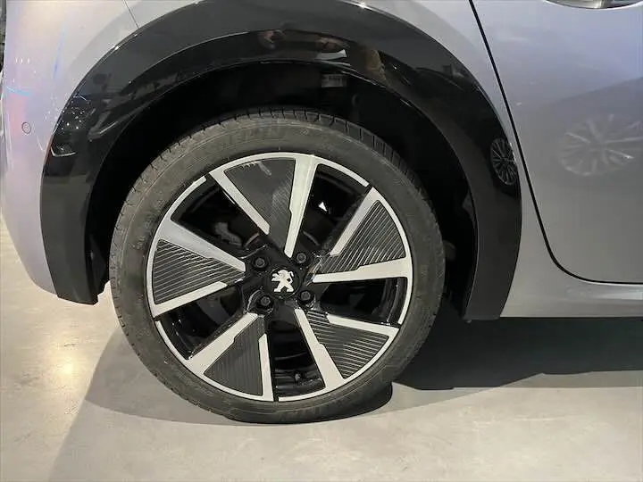 Gros plan sur la roue avant gauche de la Peugeot e-208 GT gris Artense avec jante alliage noire et argentée.