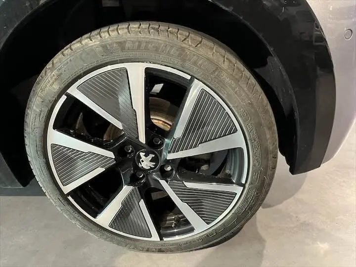 Gros plan sur la jante avant droite de la Peugeot e-208 GT gris Artense, avec son design moderne bicolore noir et argent.